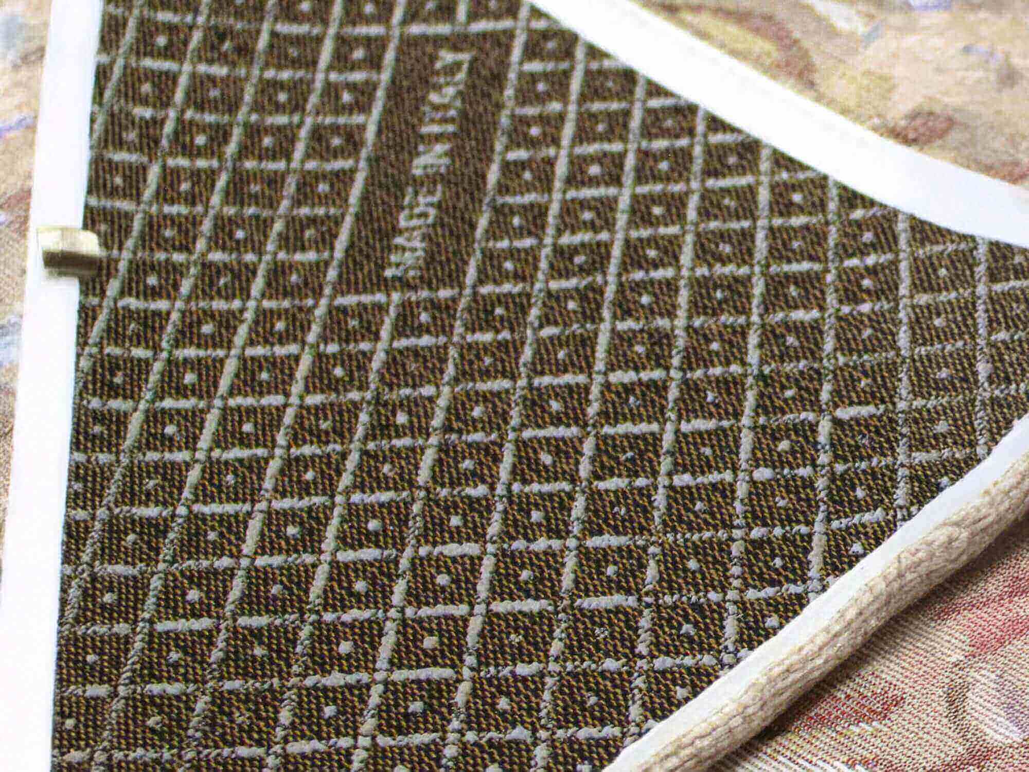 Primo piano di un campione di tessuto con texture in tonalità marroni e motivo geometrico.