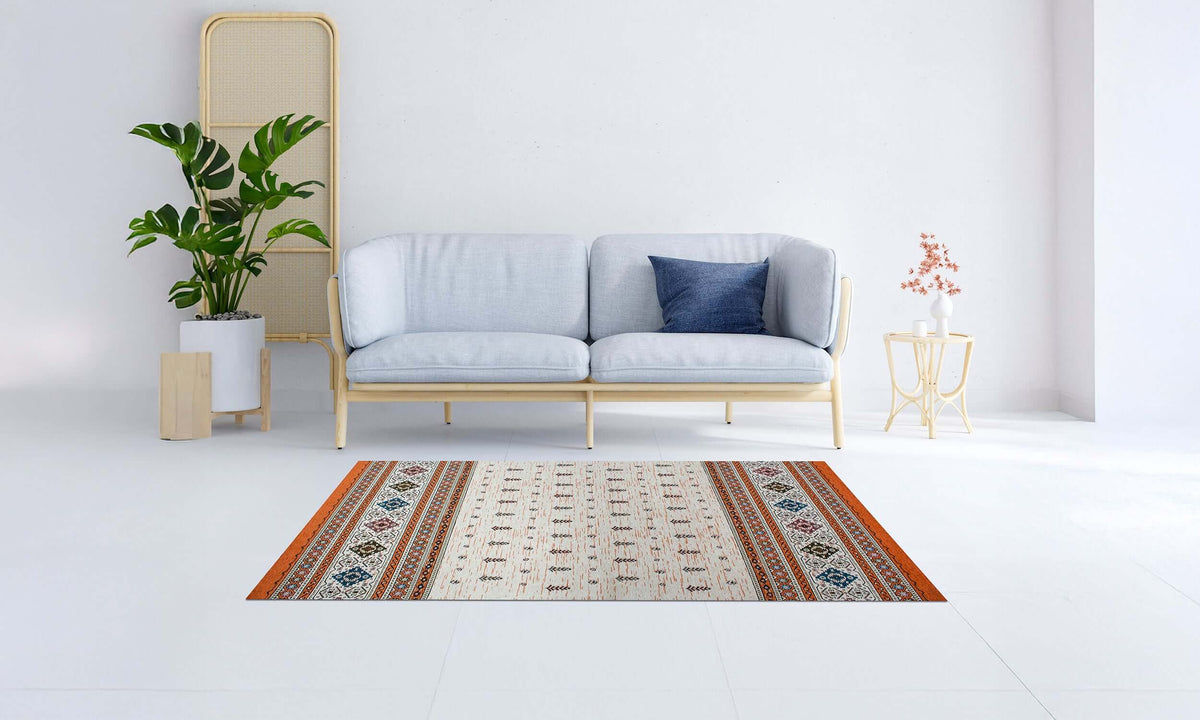TAPPETO ARREDO LOOM RUGGINE 115x175 cm su pavimento bianco con divano moderno e pianta decorativa.
